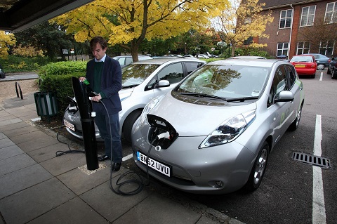 A man is connecting charging cable from a Nissan LEAF to a charging point at a car park