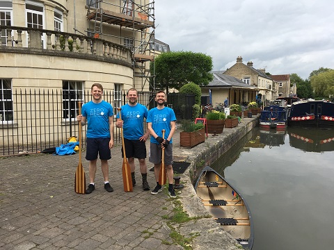 Three smiling  men with oars next to a canal