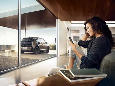 A lady browsing her mobile phone while BMW-i3 is charging outside