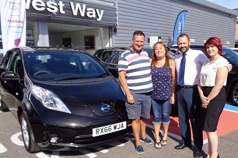 Four people standing in front of cars at a dealership